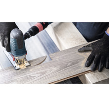 Eine Stichsäge schneidet ein Laminatbrett. Schutzhandschuhe werden getragen.