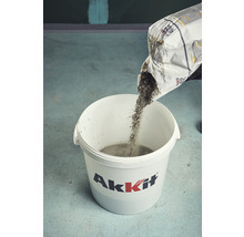 Eine Person gießt Trockenbetonmischung aus einer Tasche in einen Eimer.