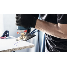 Eine Stichsäge schneidet eine Linie in ein Werkstück. Der Benutzer trägt Handschuhe.