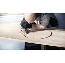 Mann sägt mit einer Stichsäge ein Loch in eine Holzplatte.