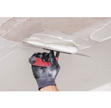 Hand mit Spachtel trägt Spachtelmasse auf die Decke auf.