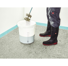 Mörtel wird in einem Eimer mit einem Rührwerk gemischt, getragen werden Gummistiefel und eine Arbeitshose.
