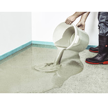 Eine Person gießt Ausgleichsmasse aus einem Eimer auf einen Boden.