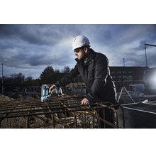 Ein Bauarbeiter mit Schutzhelm verwendet einen Akku-Bindeautomat auf einer Baustelle.