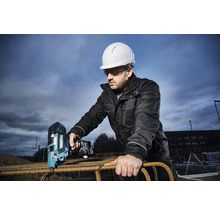 Mann mit Schutzhelm und Schutzbrille bedient einen Akku-Bindedrahtautomaten von Makita auf einer Baustelle zum Verarbeiten von Bewehrungsstahl.