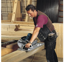 Ein Mann sägt einen Holzbalken mit einer Handkreissäge in einer Werkstatt.