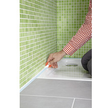 Abdichten einer Duschwanne mit Silikon im Badezimmer mit grünen Fliesen.