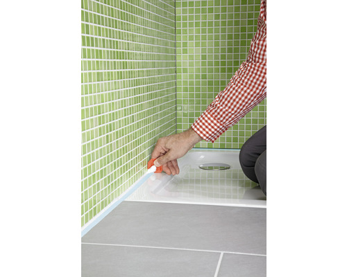 Abdichten einer Duschwanne mit Silikon im Badezimmer mit grünen Fliesen.