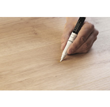 Eine Hand verwendet einen Retuschierstift auf einer Holzoberfläche.