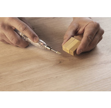 Person repariert Holzboden mit Reparaturwachs und Schmelzgerät