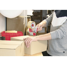 Eine Person verschließt einen Karton mit einem Handabroller.
