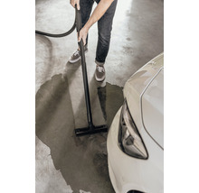 Eine Person reinigt mit einem Nass Trockensauger eine Wasserlache neben einem Auto auf einem Garagenboden.