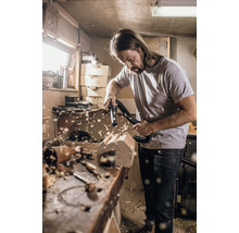 Mann saugt Holzstaub von einer Holzskulptur mit einem Staubsauger in einer Werkstatt.