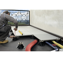 Mann verlegt Terrassenplatten auf einem Balkon mit Hilfe von Stelzlagern