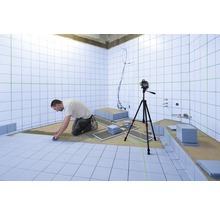 Ein Mann verlegt Fliesen in einem Badezimmer, wobei ein Laser-Nivelliergerät verwendet wird, um die Ausrichtung zu gewährleisten.