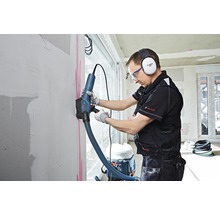 Handwerker mit Mauernutfräse beim Bearbeiten einer Wand. Staub wird abgesaugt.