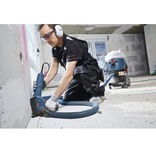 Handwerker nutzt eine Mauernutfräse mit Staubsauger auf einer Baustelle.