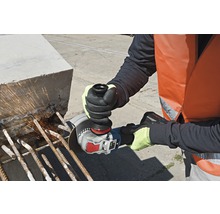 Ein Arbeiter mit Schutzweste und Handschuhen schneidet mit einem Winkelschleifer Stahlstäbe in einem Betonblock.