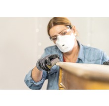 Frau schleift Holz mit Schleifpapier, Schutzbrille und Atemschutzmaske