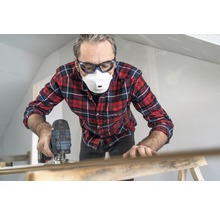 Mann arbeitet mit einer Stichsäge, trägt dabei Schutzbrille und Staubmaske.