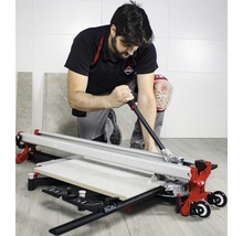 Ein Handwerker kniet und schneidet eine Fliese mit einem Fliesenschneider.