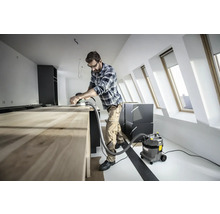 Handwerker schleift Holztisch mit Schleifgerät und Staubsauger in heller Dachgeschosswohnung.