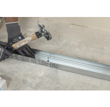 Handwerker befestigt Trockenbauprofil mit Hammer und Handschuhen.