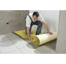 Ein Mann verlegt eine Entkopplungsmatte auf einem gefliesten Boden.