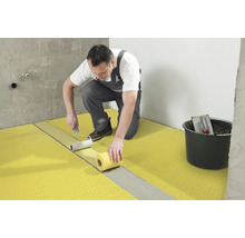 Handwerker bringt mit einer Farbwalze eine Abdichtungsbahn auf den Boden auf. Im Hintergrund ist ein Eimer mit Werkzeugen zu sehen.