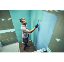 Mann streicht eine Wand mit einer Farbrolle in einem Badezimmer