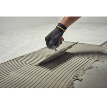 Fliesenleger trägt mit einer Kelle Klebstoff auf den Boden auf