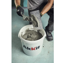 Handwerker entnimmt Fliesenkleber mit einer Kelle aus einem Eimer von Akkit