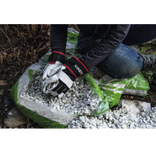 Person befüllt Sack mit Zierkies mit Gartenhandschuhen