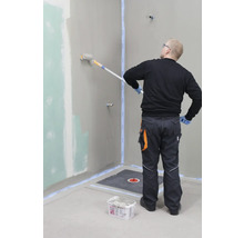 Handwerker beschichtet eine Badezimmerwand mit einer Farbrolle. Vorbereitetes Badezimmer mit Abdichtung und Duschablauf.