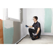 Ein Mann streicht eine Wand mit einer Farbwalze in einem Raum.