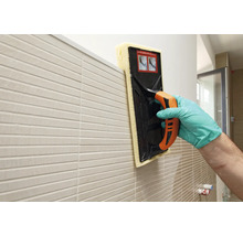 Fliesenleger reinigt eine Wand mit einem Fugenschwammbrett.