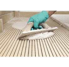 Hand mit Handschuh und Glättkelle beim Verlegen von Fliesen