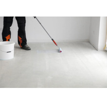 Ein Arbeiter grundiert einen Boden mit einer Walze in einem Raum.