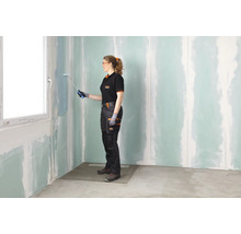 Eine Frau streicht eine Wand mit einer Farbrolle in einem Raum mit Gipskartonplatten.