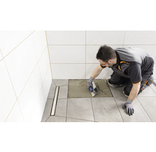 Fliesenleger trägt Kleber auf Bodenfliese im Badezimmer auf