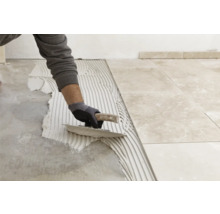 Fliesenleger trägt Kleber auf Boden auf