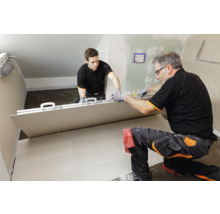 Zwei Handwerker verlegen eine große Fliese im Innenraum.