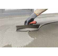 Fliesenleger mit Zahnspachtel beim Auftragen von Klebstoff