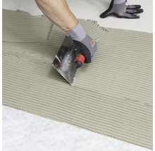 Fliesenleger trägt mit einer Kelle Fliesenkleber auf einen Untergrund auf