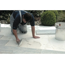 Handwerker verlegt Fliesen im Außenbereich mit einer Glättkelle und Fliesenkleber.