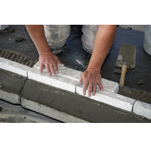 Handwerker verlegt Bordsteine mit Mörtel und Kelle