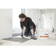 Frau verlegt Fliesen mit Fliesenkleber der Marke PCI