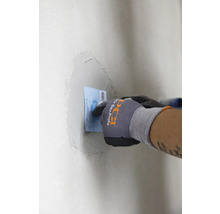 Person verspachtelt eine Wand mit einem Spachtel