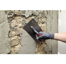 Maurer verputzt mit einer Glättkelle eine Wand.