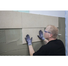 Fliesenleger bei der Arbeit: Anbringen einer Wandfliese im Badezimmer.